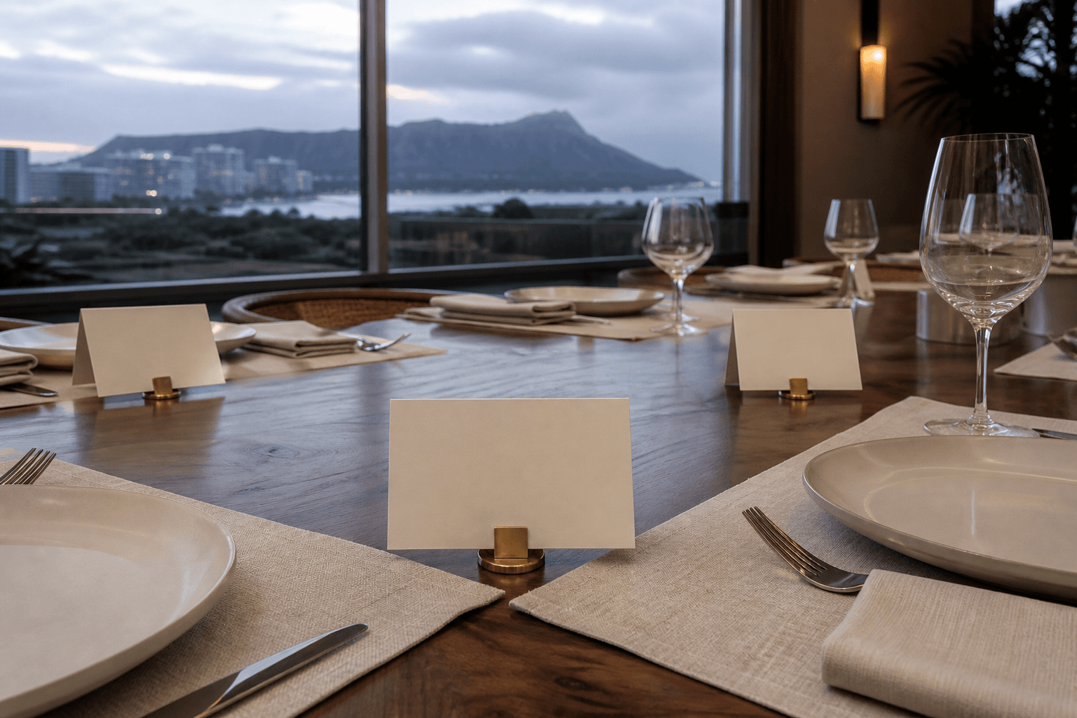 A Kahala dining table at dusk with blank cream place cards, brass clip, Diamond Head faint.