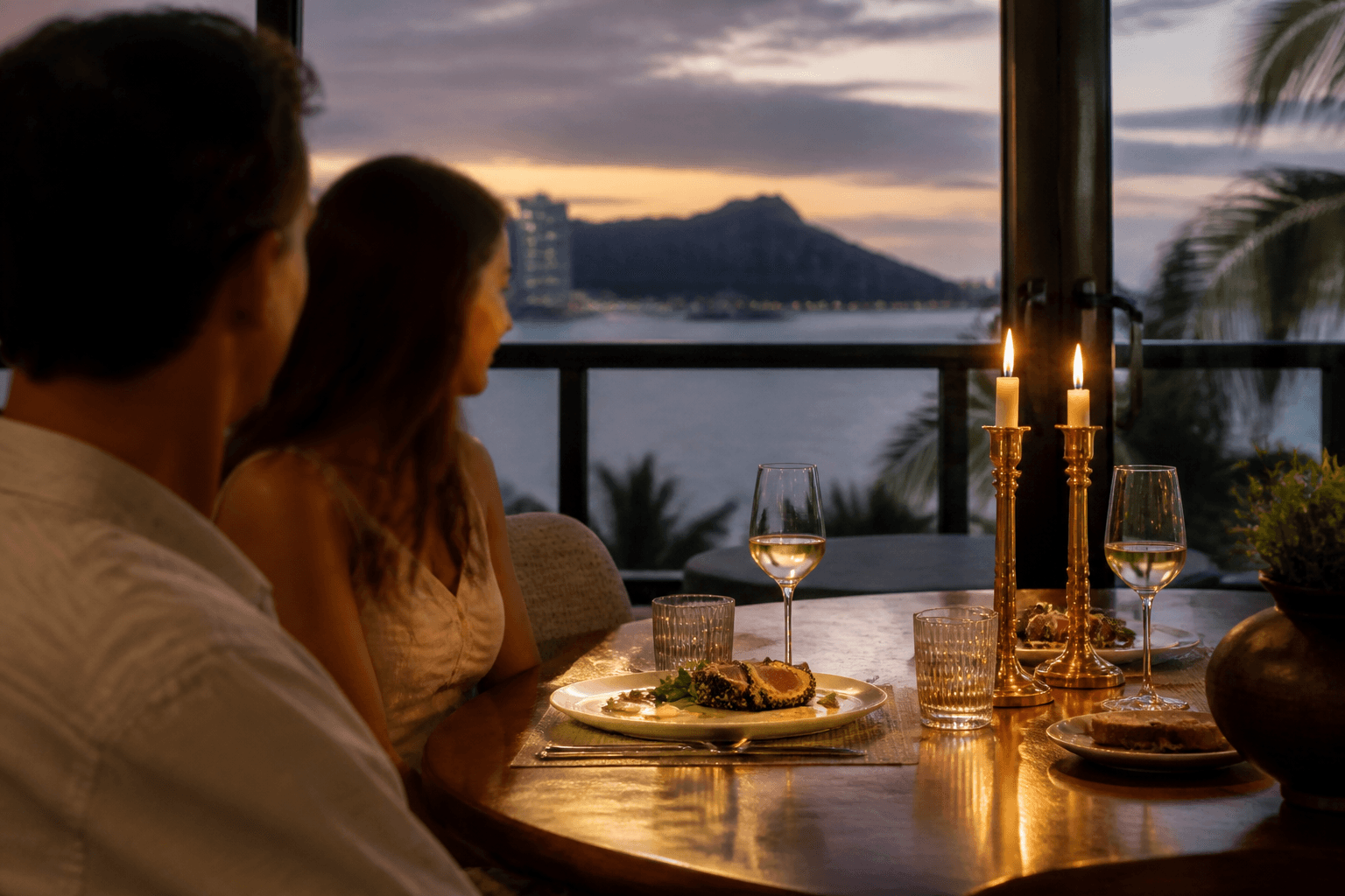 Two seats at a Kahala dining table at dusk — plated ahi, brass, Diamond Head faint.