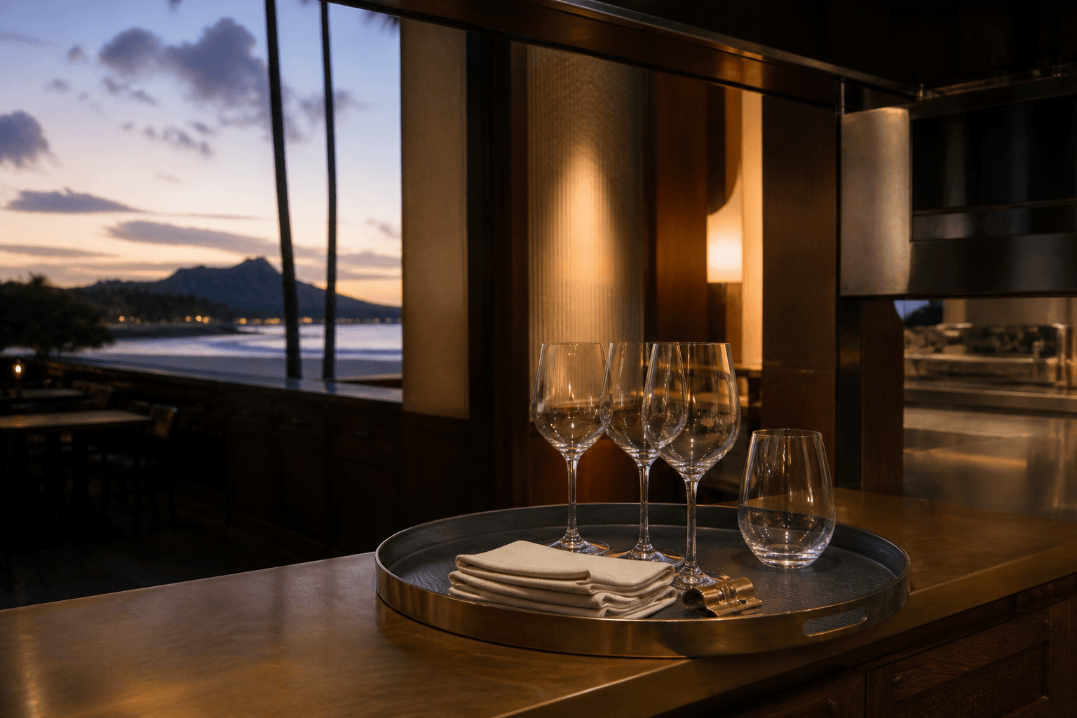 Unused empty stemware and sand linen on a Kahala kitchen pass at dusk, brass clip.